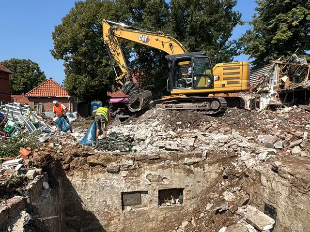 Bagger mit Sortiergreifer auf einer Abbruchstelle, im Hintergrund ein Teilabriss