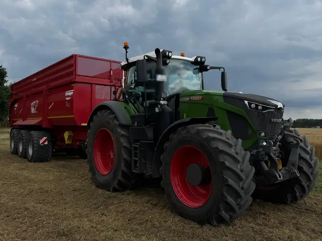 Fendt-Traktor mit rotem Kippanhänger auf einem abgeernteten Feld unter dramatischem Himmel