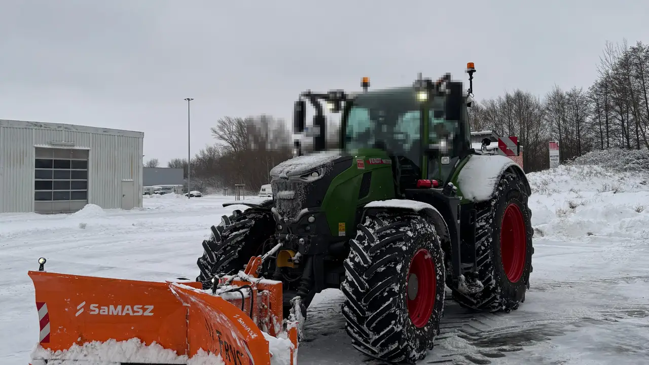 Traktor mit orangem Schneeschild räumt eine verschneite Fläche
