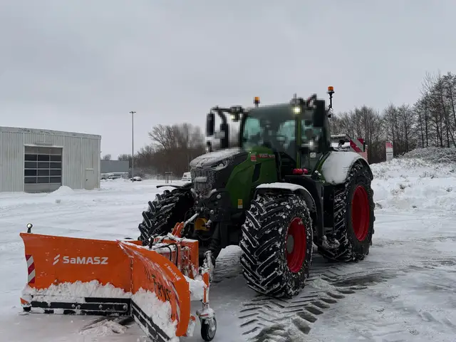 Traktor mit orangem Schneeschild räumt eine verschneite Fläche